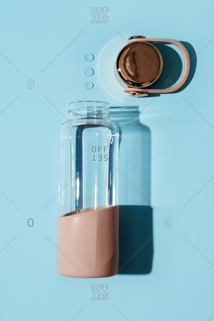 High angle view of an empty reusable bottle and some water drops on a blue background