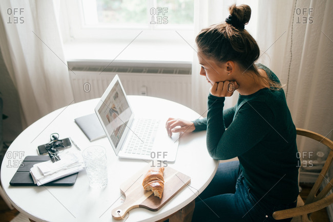 Side view of woman reading food recipe on laptop at table in living room