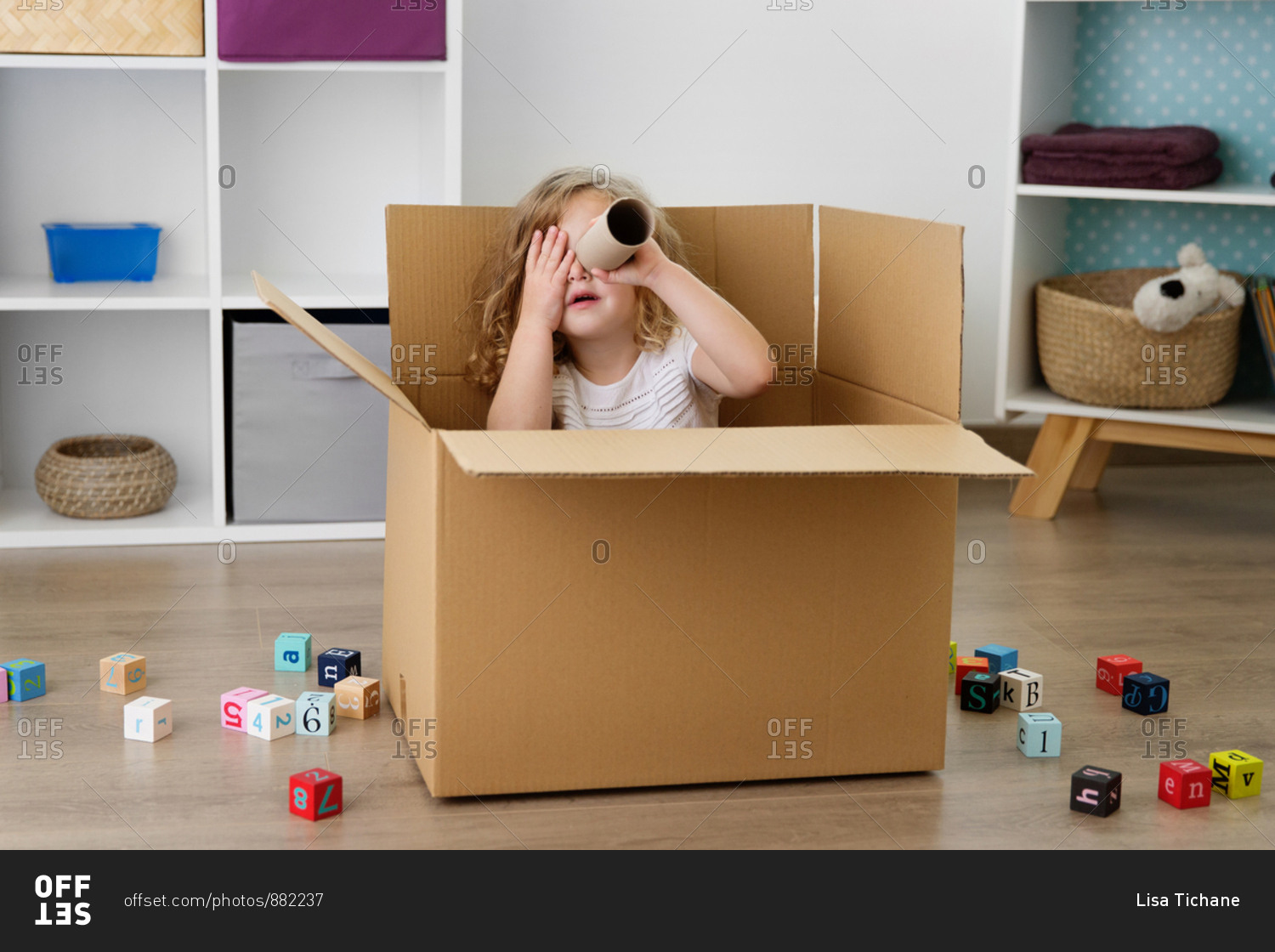 Playful girl looking through cardboard tube while sitting in box