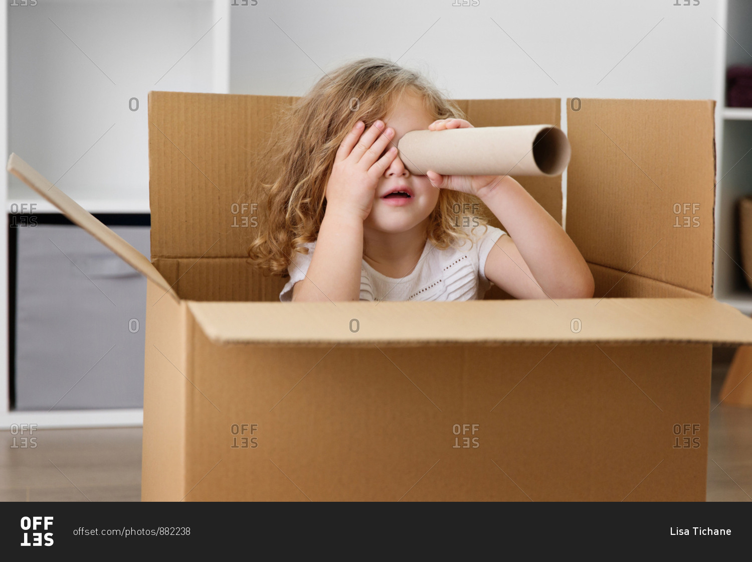 Young girl looking through cardboard tube while sitting in box