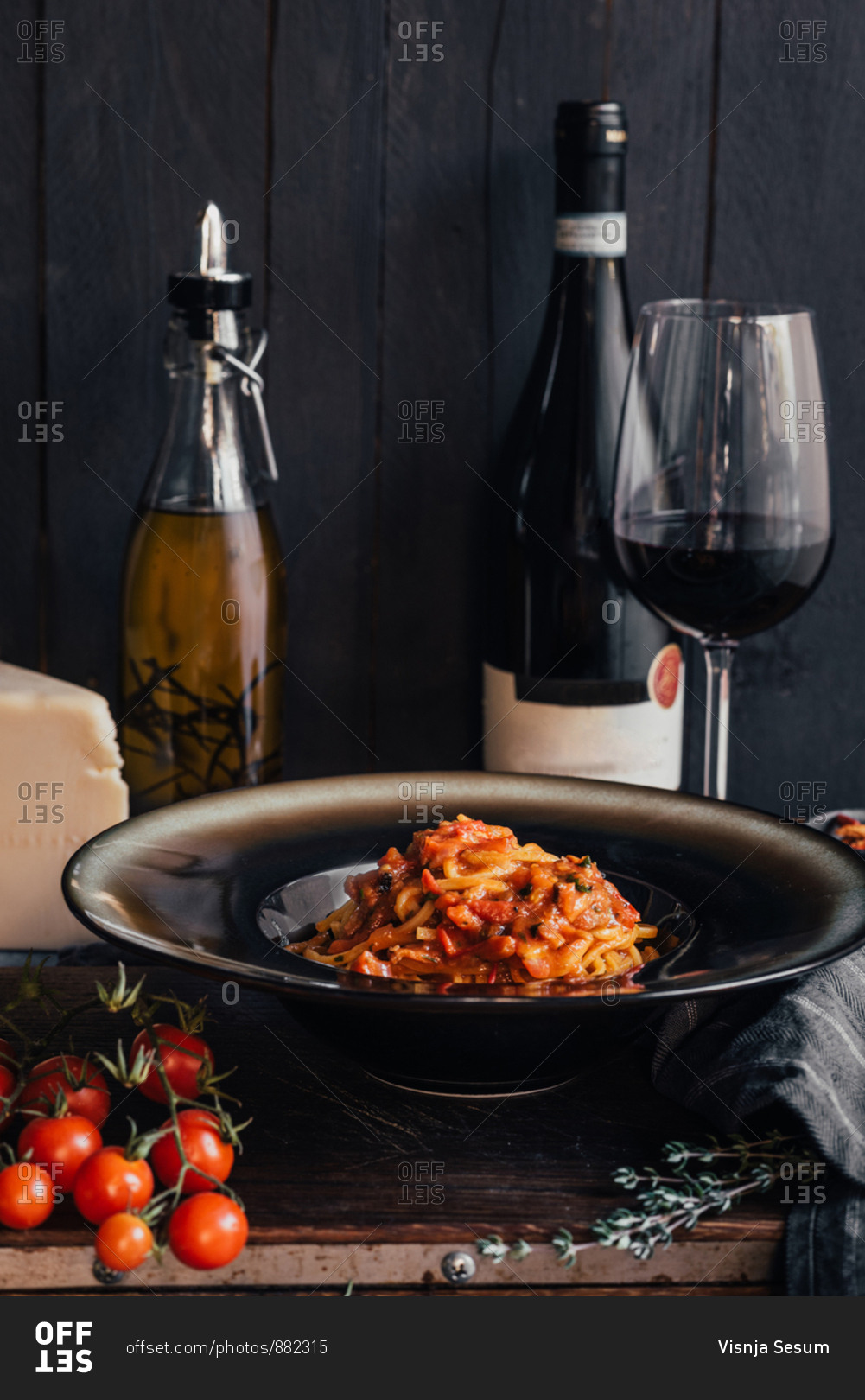 Homemade pasta with tomato sauce in a plate next to a bottle of red wine