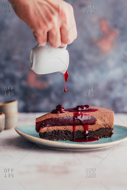 Hand pouring raspberry sauce over a piece of chocolate cake