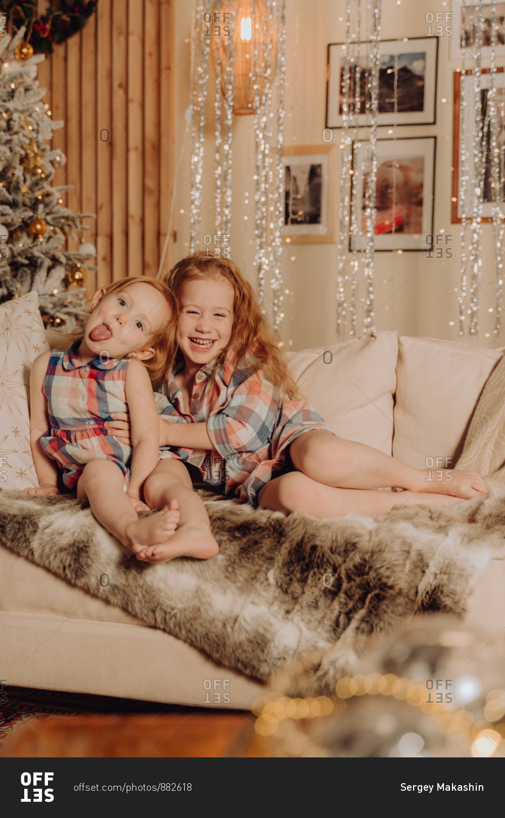 Two sisters playing and hugging on the couch with holiday lights in the background