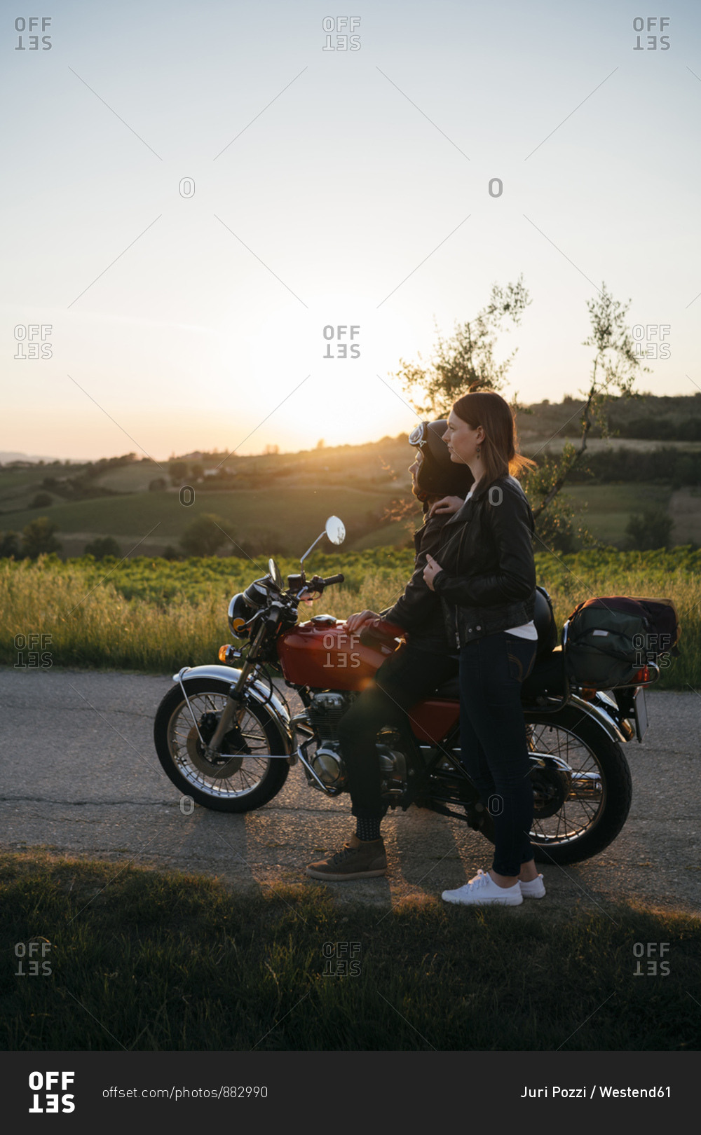 Young couple with vintage motorbike standing on country road at sunset looking at view- Tuscany- Italy