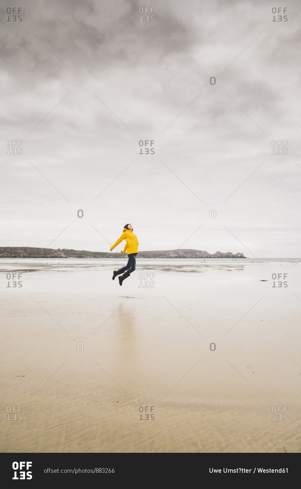 Young woman wearing yellow rain jacket at the beach- Bretagne- France