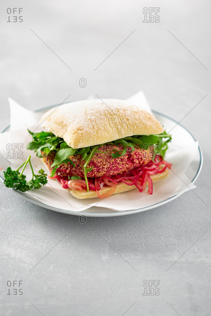 Vegetarian burger with beetroot patty, fermented onions and arugula on white background