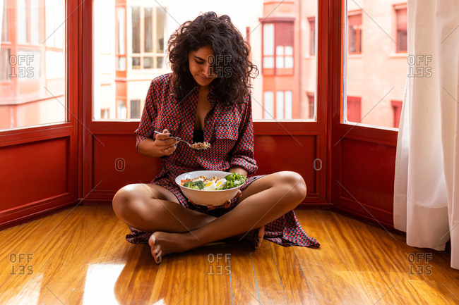Latin woman eating a healthy while lunch sitting on the floor at home