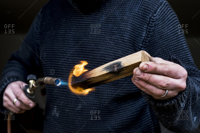 Close up of man holding blowtorch, charring wooden handle of a knife.
