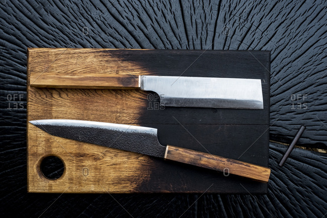 High angle close up of two handmade knives on wooden cutting board.