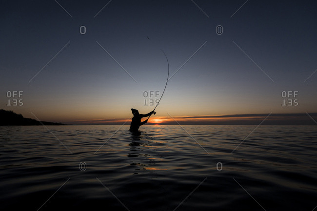 Angler fishing in the baltic sea at sundown standing in water.
