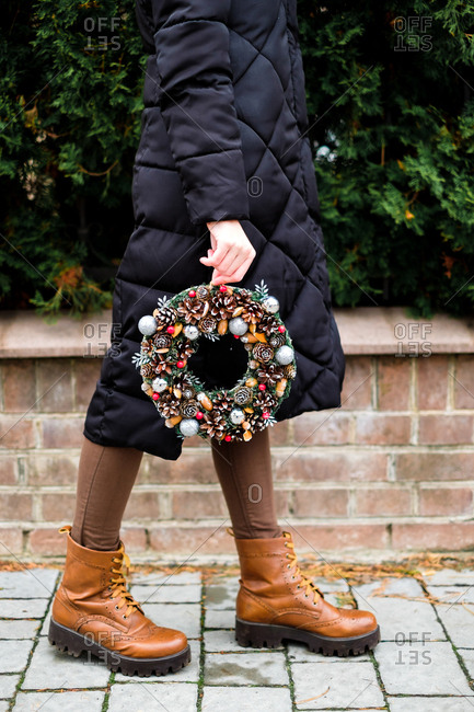 The pretty girl is holding colorful handmade Christmas wreath with cones and glistening balls in her hands