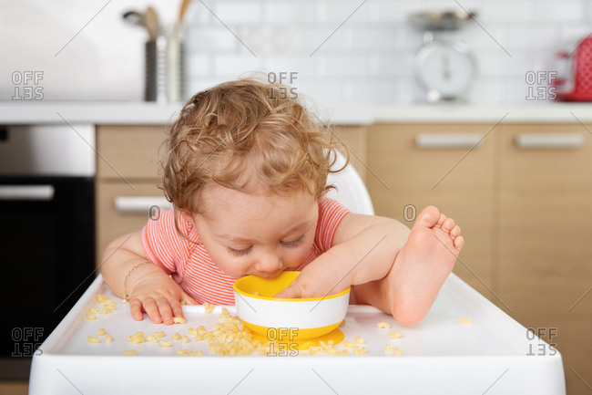 Baby in high chair eating pasta straight from bowl