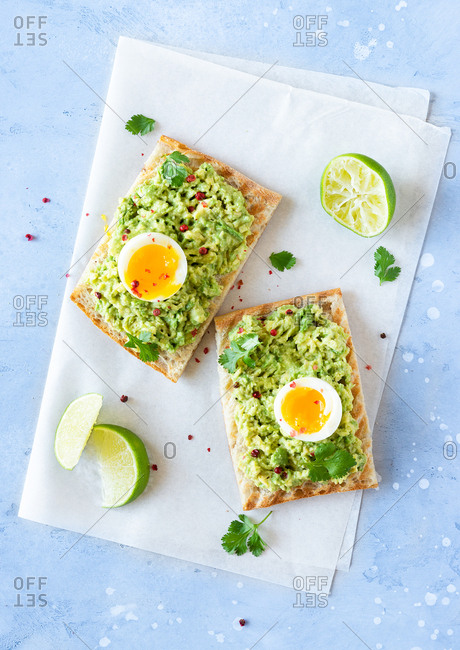 Overhead view of avocado toast with soft-boiled eggs and lime