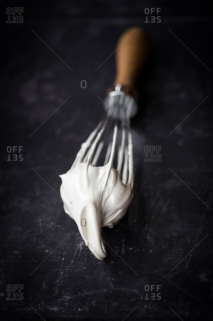 Close up of a hand balloon whisk with beaten egg white meringue on black background