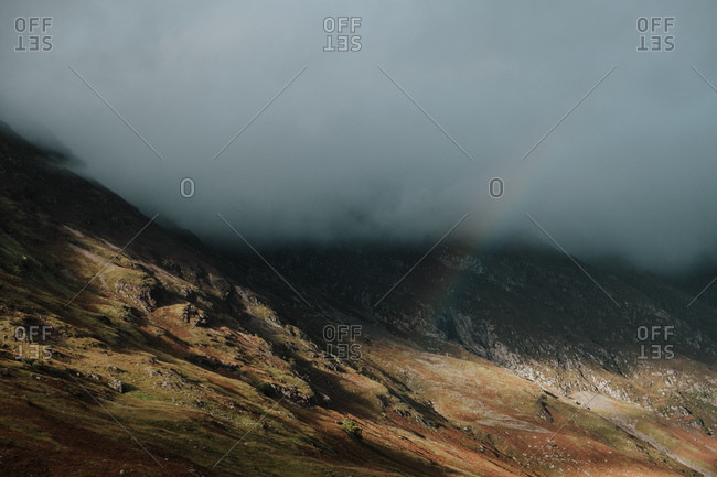 Wilderness scenery of rocky hills covered by thick mist and dim rainbow in Scotland