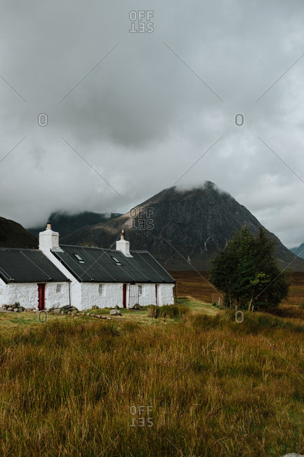 Lonely white farmhouse in autumn field in valley in Scotland surrounded by rocky hills