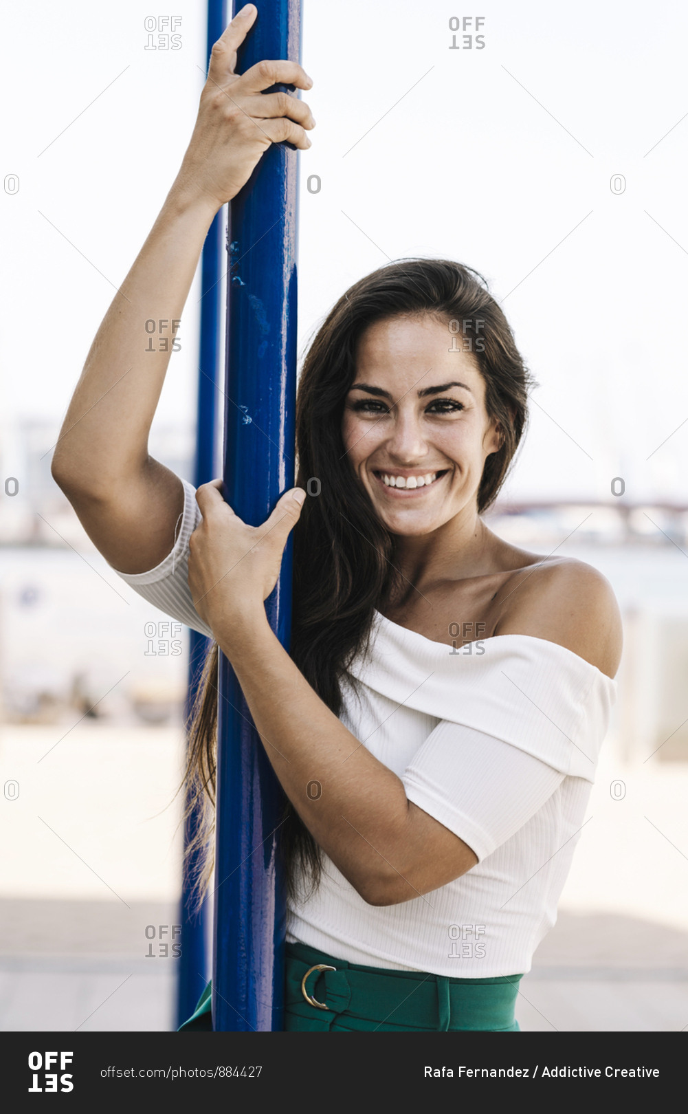 Beautiful smiling young woman hanging on a pole in the street while looking camera