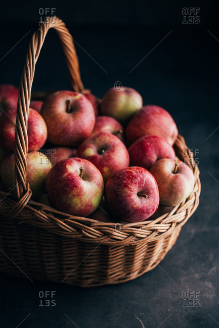 Fresh red apples on dark table and in a wicker basket on dark background