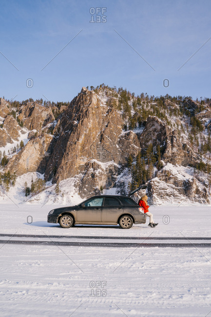 Woman sitting on car trunk in snowy valley