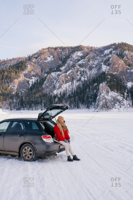 Woman sitting on car trunk in snowy valley