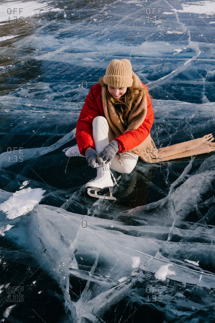 Woman sitting on frozen river and tying the shoelaces