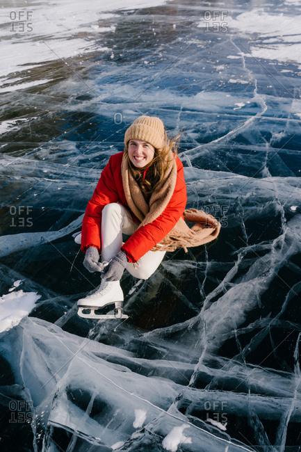 Woman sitting on frozen river and tying the shoelaces