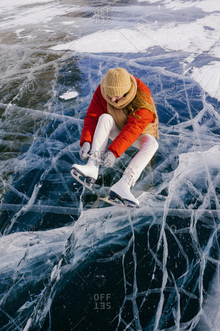 Woman sitting on frozen river and tying the shoelaces