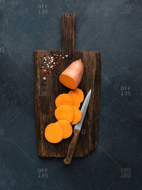 Raw sweet potato on wooden cutting board with salt and pepper