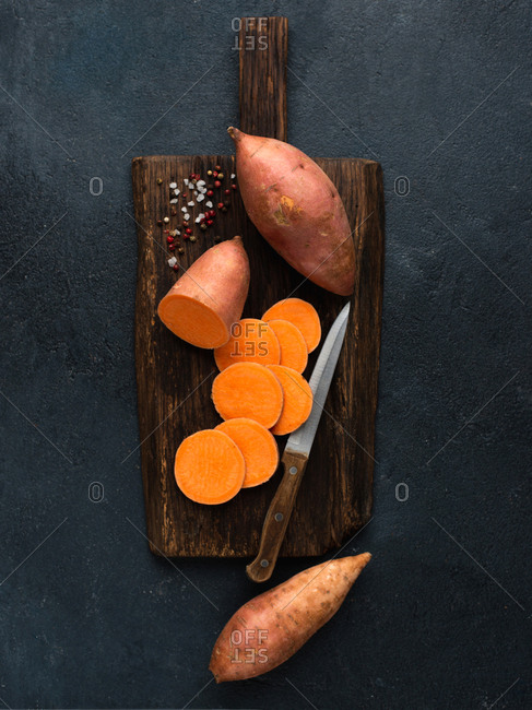 Raw sweet potato on wooden cutting board with salt and pepper