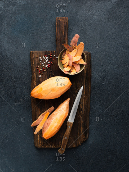 Peeled sweet potato on wooden cutting board with salt and pepper
