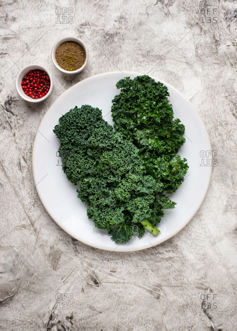 Overhead view of fresh kale leaves on ceramic plate and spices