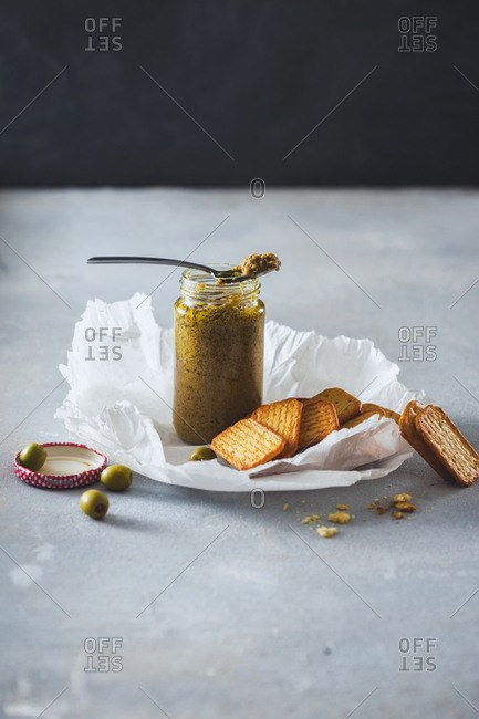 Olive pesto in jar with crackers on light background