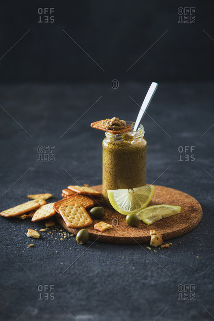 Olive pesto in jar with crackers on dark background