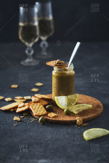 On dark background olive pesto in jar with crackers