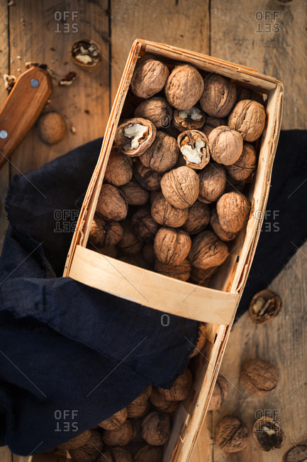 Whole walnuts and walnut pieces in wicker basket on wooden table