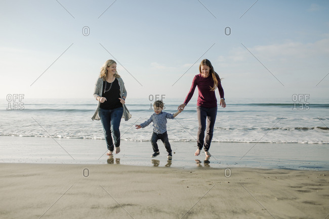 Happy lesbian mothers and son walking at beach against sky
