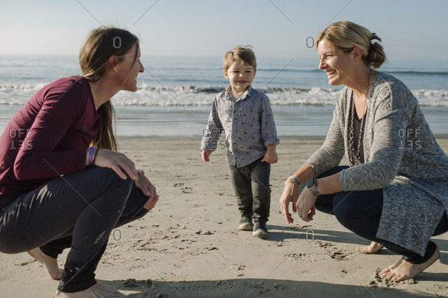 Lesbian couple looking face to face with son standing at beach against sea