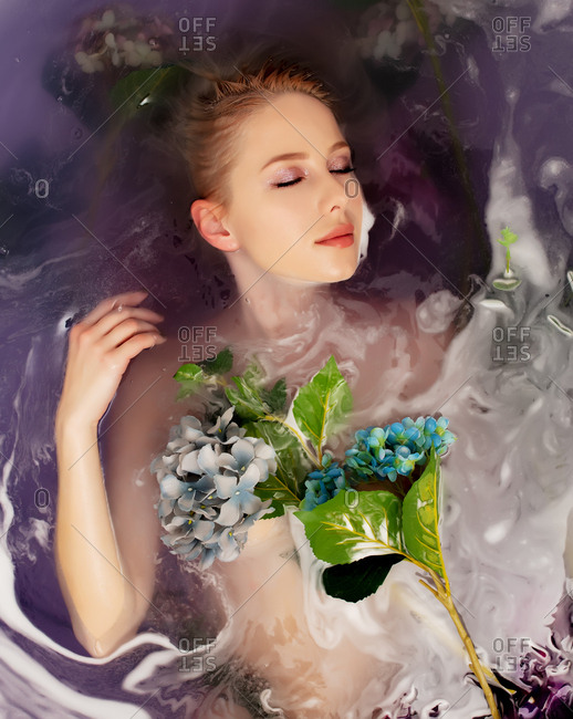 Beautiful woman covered in flowers lying in a bath tub filled with purple water