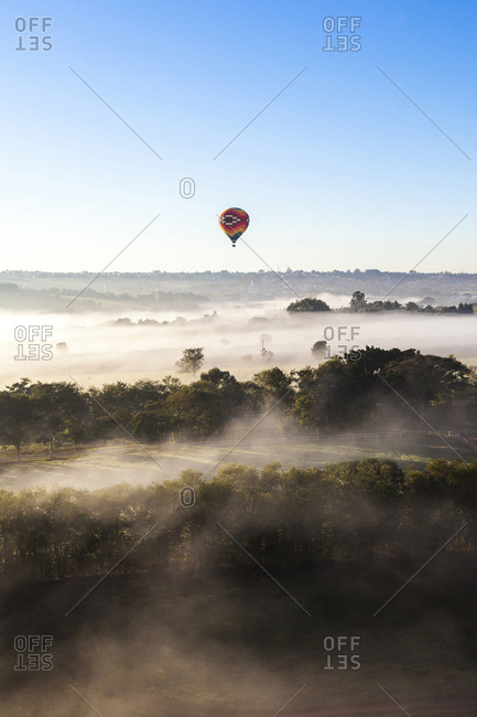 Hot air balloon flying over landscape against clear sky during foggy weather