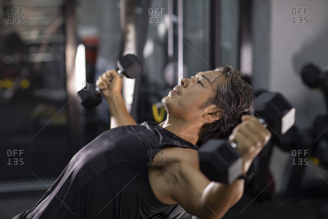 Mature Chinese man working out with hand weights at gym