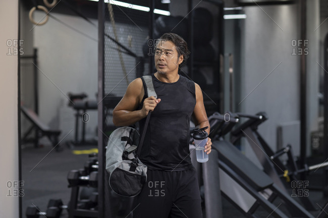 Mature Chinese man with gym bag at gym
