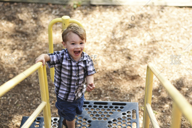 High angle view of playful boy shouting while standing on outdoor play equipment at playground