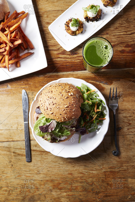 High angle view of burger with arugula served in plate by juice and french fries on wooden table