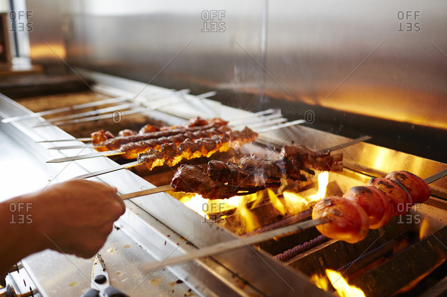 Cropped hand of chef making kebab on barbecue grill in commercial kitchen