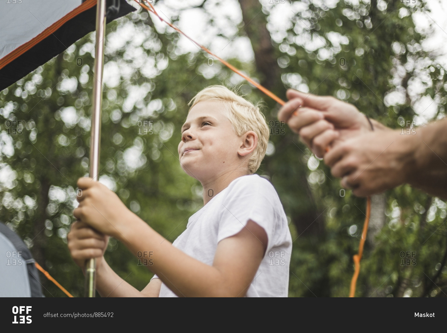 Smiling boy assisting father in pitching camping tent