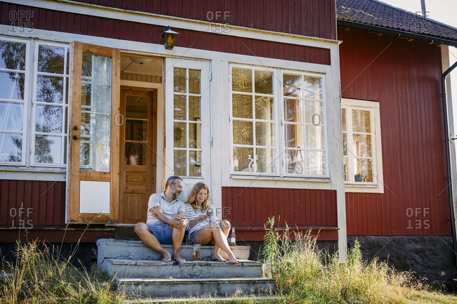 Couple looking at smart phone while sitting on steps outside log cabin