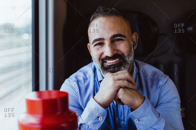 Portrait of smiling businessman with hands clasped sitting in train