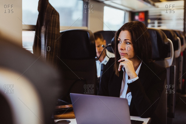 Thoughtful business commuter using laptop while looking away in train