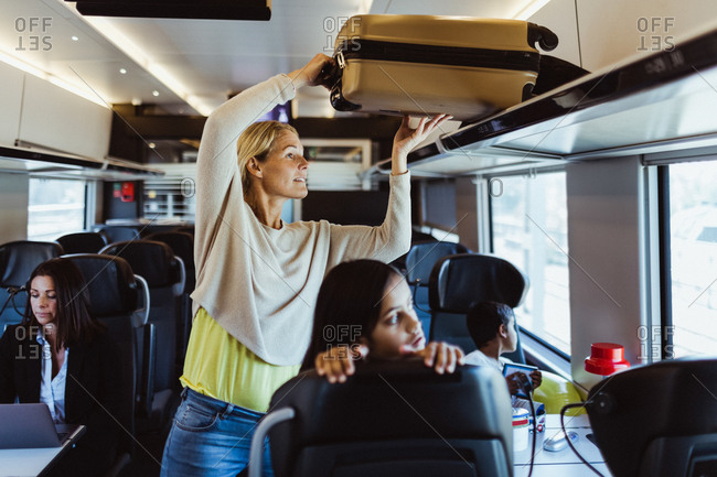 Woman arranging luggage on shelf while traveling with children in train