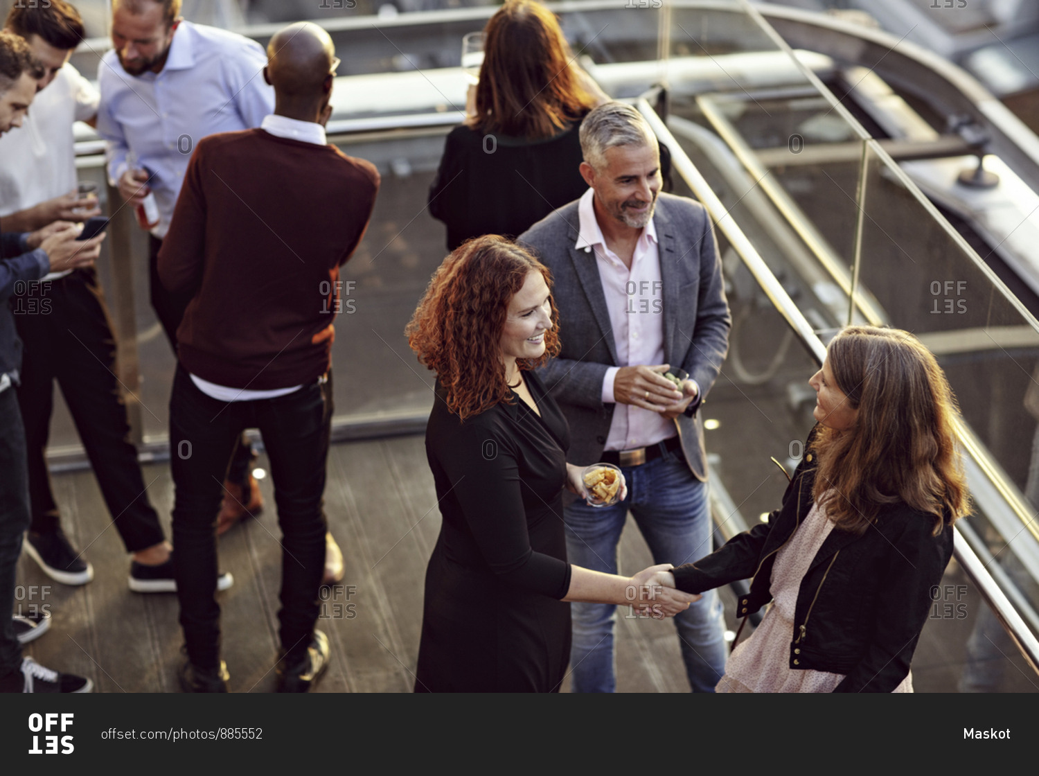 High angle view of businesswoman doing handshake and greeting while partying with coworkers after work on terrace